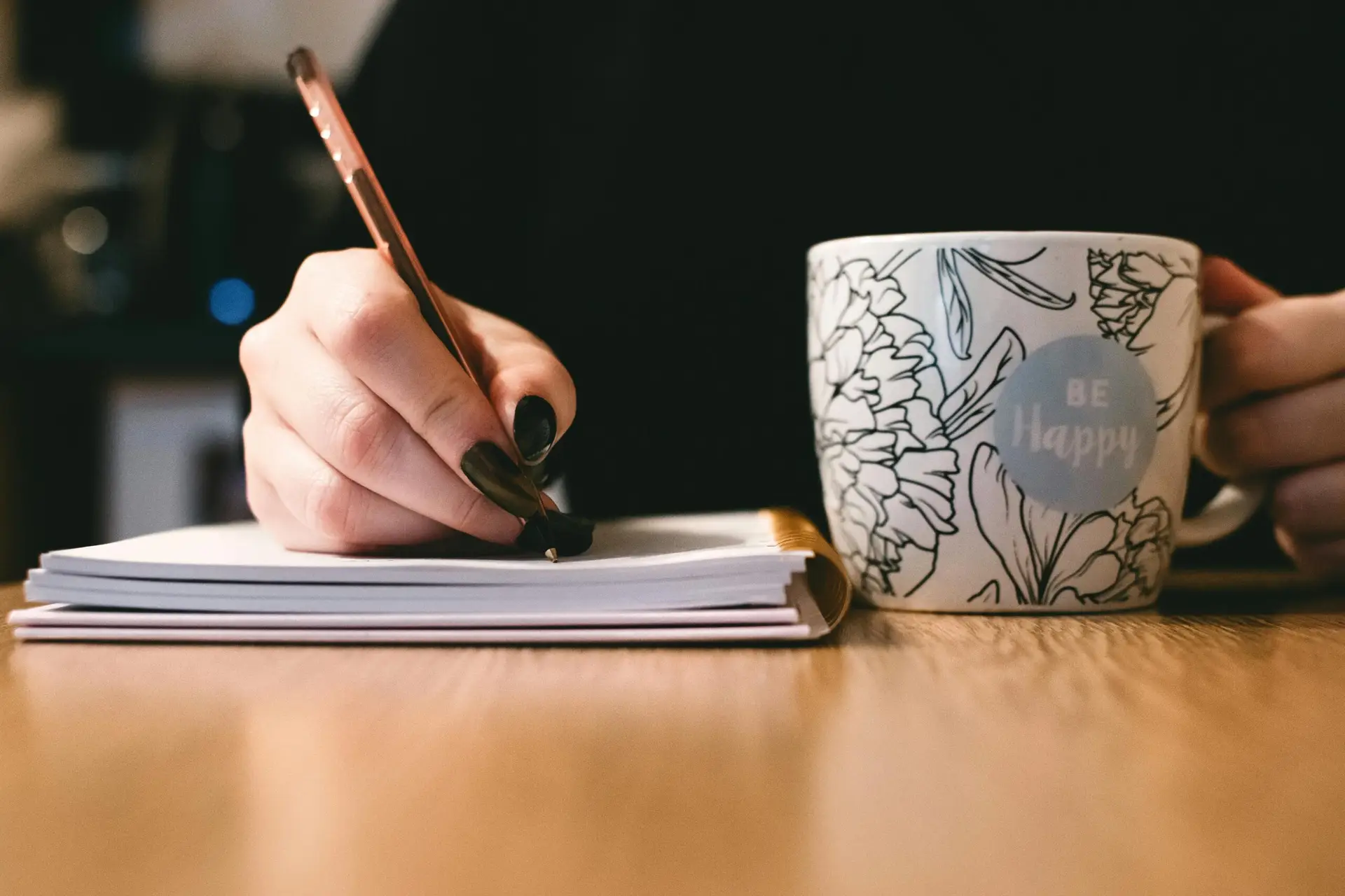 Hand schreibt Gedanken in ein Notizbuch, daneben eine Tasse Kaffee